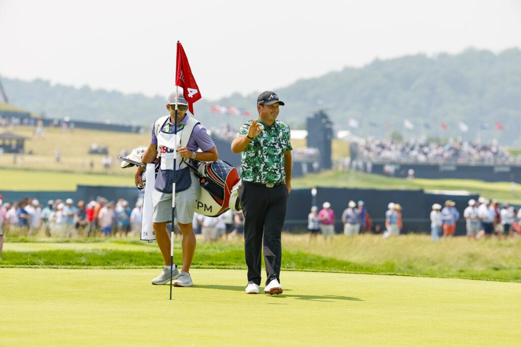 Patrick Reed takes ball out of the fourth hole after making an eagle with caddie, Kessler Karain.